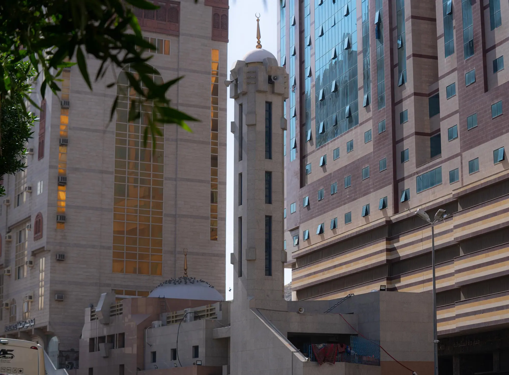 A close-up view of the modern architectural minaret of Masjid Al-Jinn in Makkah, surrounded by tall hotel buildings.