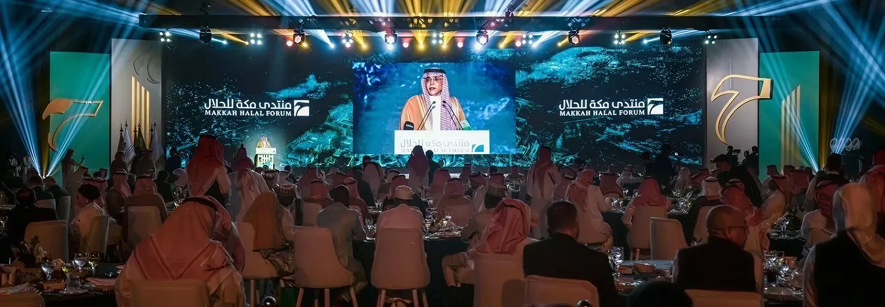 مجموعة من الأشخاص جالسين على الكراسي وعلى مسرح به شاشة كبيرة